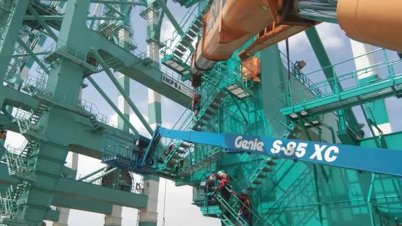 A Genie S85 telescopic boom lift rental working alongside a mobile crane at a port.