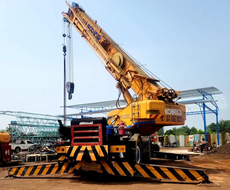 A 50-ton Kobelco rough terrain crane operating on a compact job site.
